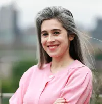 Headshot of a woman wearing a pink jumper, smiling at the camera