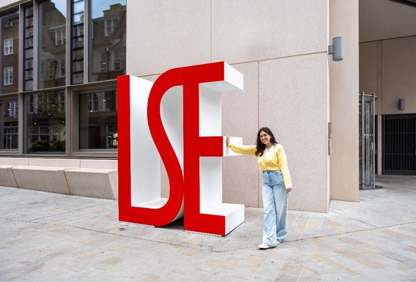 Baya standing beside the large red LSE letters on the LSE campus.