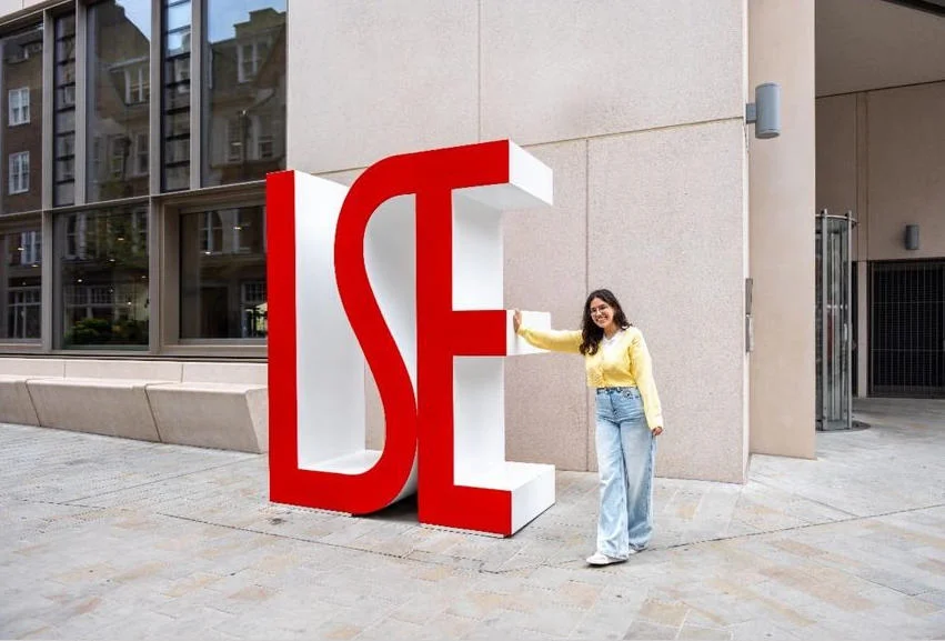Baya standing beside the large red LSE letters on the LSE campus.