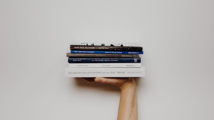 A right hand with modern books balanced flat on top against a white wall