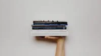 A right hand with modern books balanced flat on top against a white wall