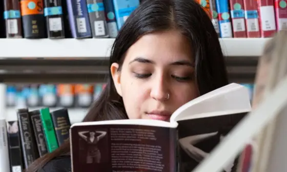 A person smiling reading a book in the stacks