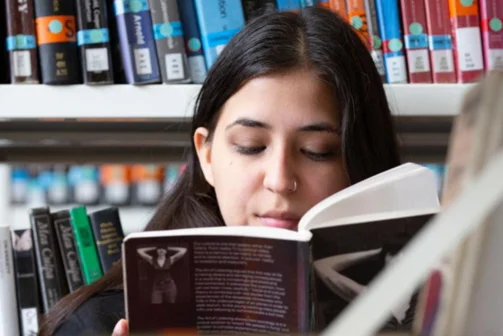A person smiling reading a book in the stacks