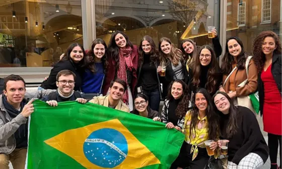 Group of students holding a Brazil flag in front of a window.