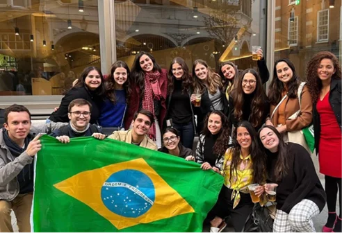 Group of students holding a Brazil flag in front of a window.