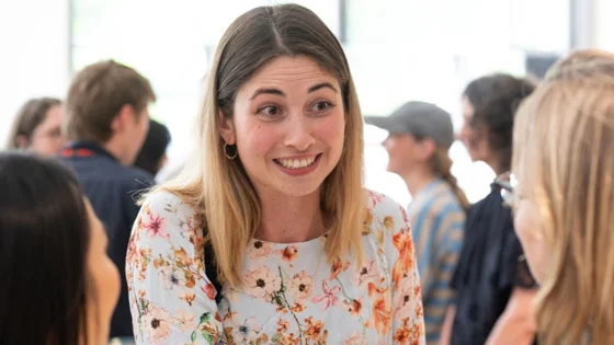 Smiling woman in a floral shirt talking with two people in a lively, casual group setting indoors.