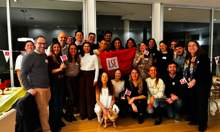 A large group of alumni gathered for a pictured with LSE flags and a dog.