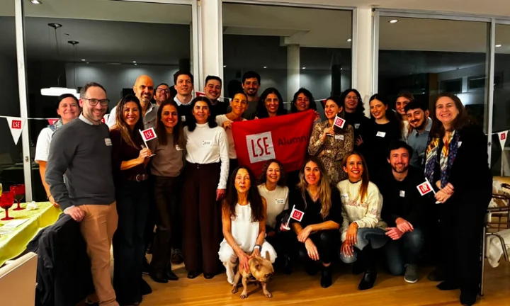A large group of alumni gathered for a pictured with LSE flags and a dog.