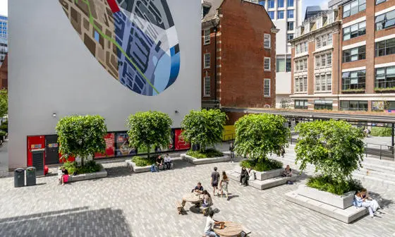 LSE Centre Buildings square on a sunny day. People sit on bences and walk through the square.