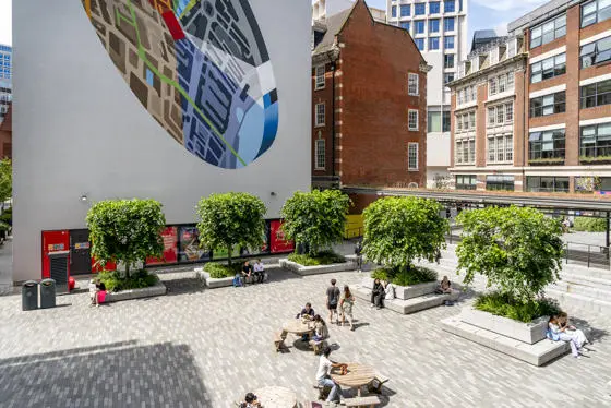 LSE Centre Building square on a sunny day. People sit on benches and walk through the square.