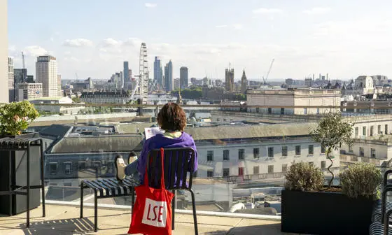Student sitting on chair on rooftop terrace facing london eye