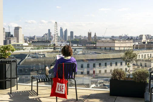 Student sitting on chair on rooftop terrace facing london eye