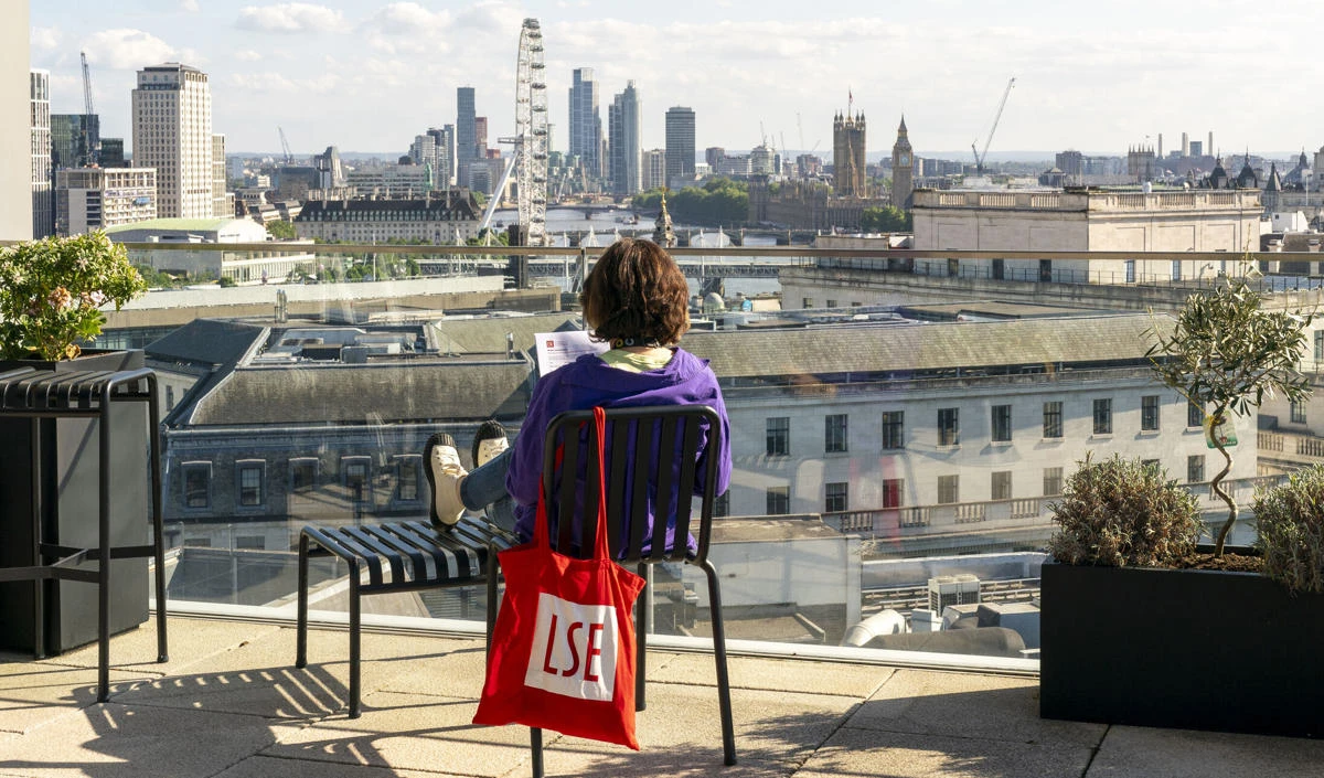 Student sitting on chair on rooftop terrace facing london eye