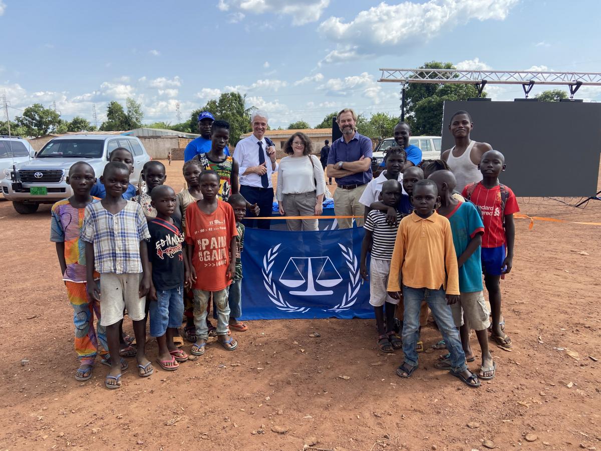 A group of children gathereed with an ICC. The flag is blue with white scales on it. 