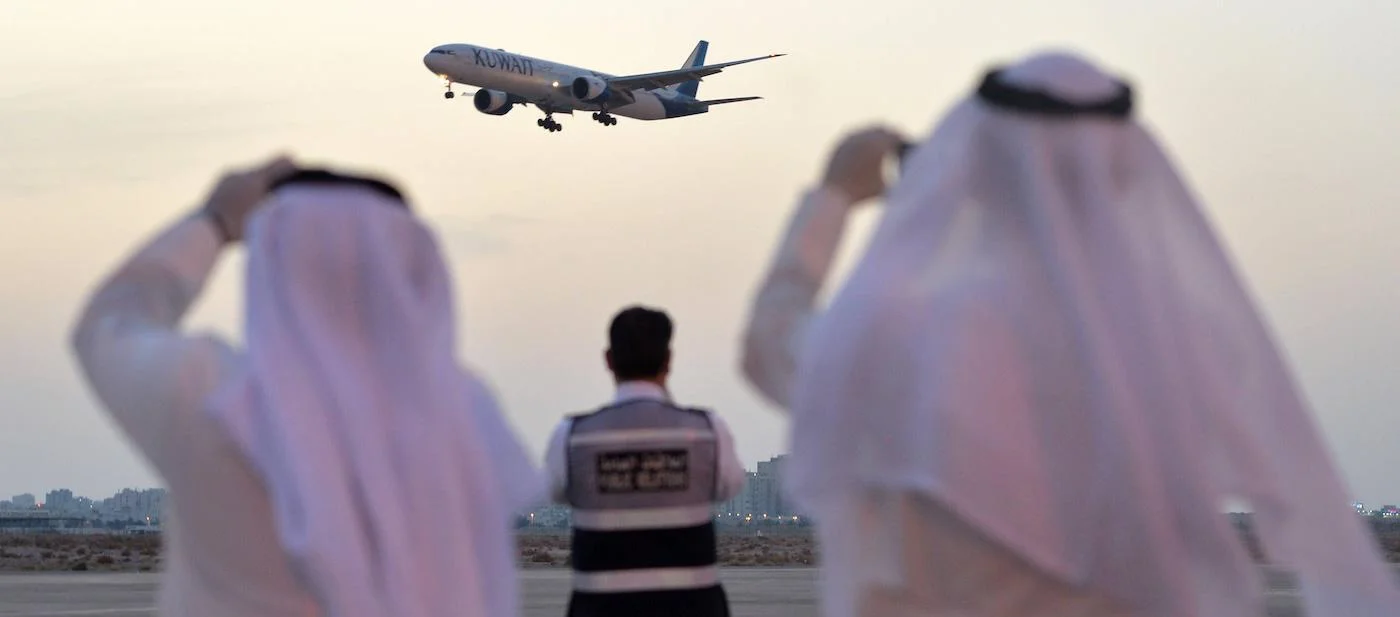 Two Kuwaiti men watching a Kuwait Airways flight taking off.