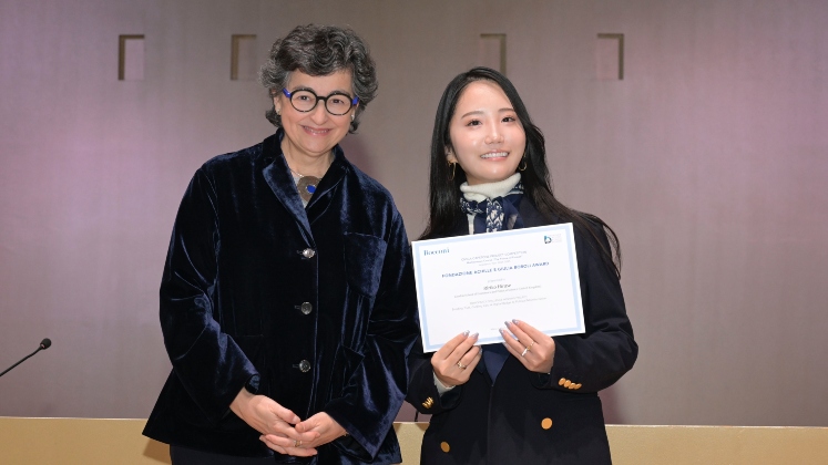 Student smiling and holding her prize certificate next to the ceremony official