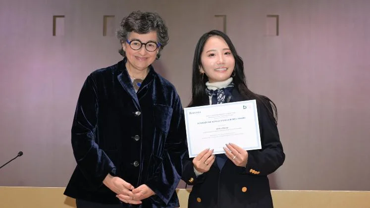 Student smiling and holding her prize certificate next to the ceremony official