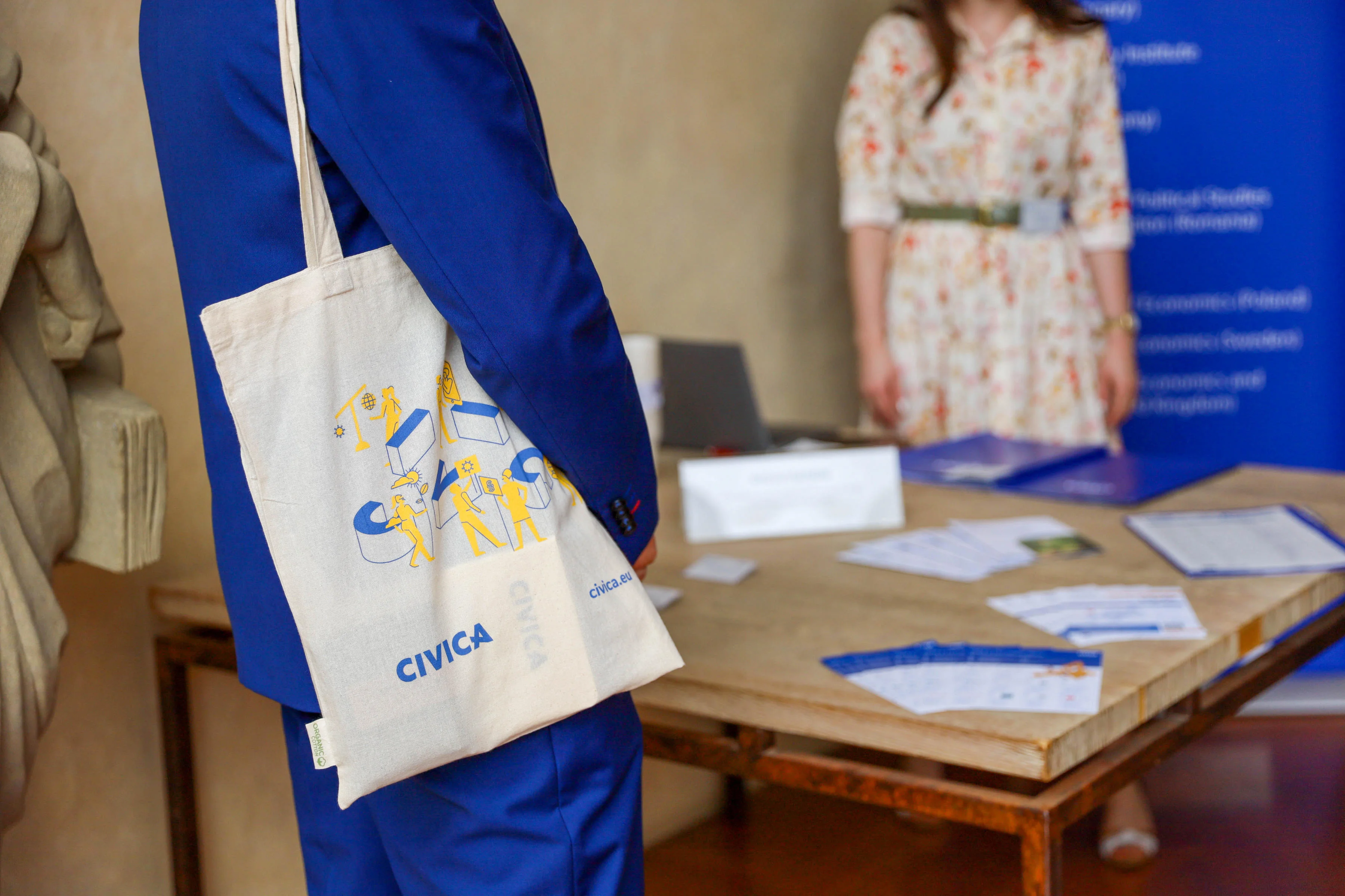 Person standing by table with leaflets and carrying a CIVICA cloth bag