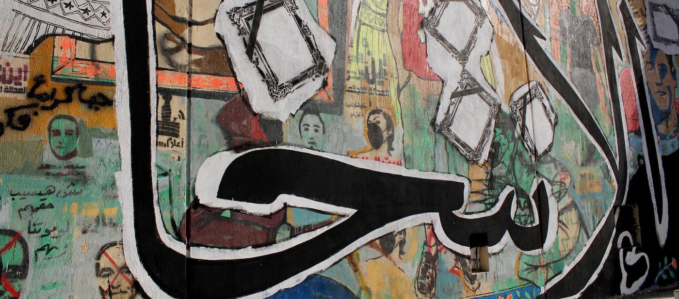 Colourful graffiti mural with portraits and Arabic text.