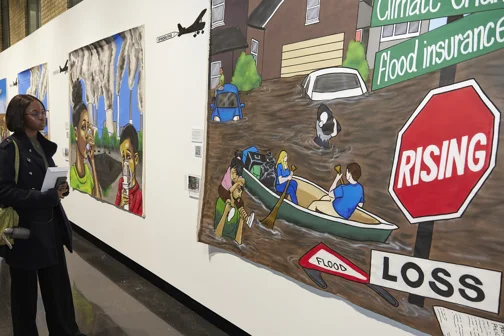 An attendee at an exhibition on climate change looking at a canvas image of flooding in the US