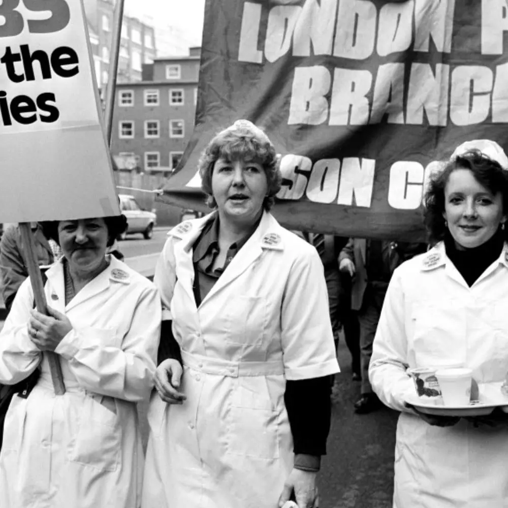 Three people on a protest march. A placard and banner are in shot.