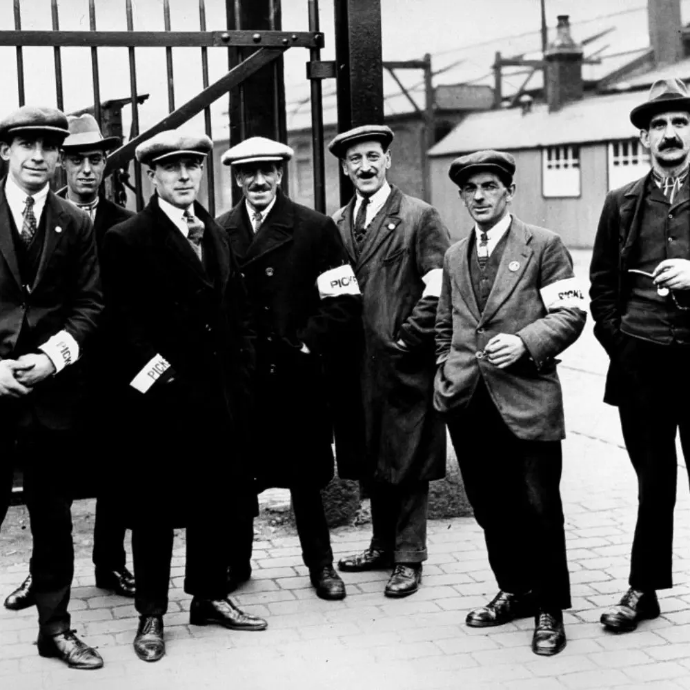 A group of men stood at a gate armbands with the word "Picket" written on.