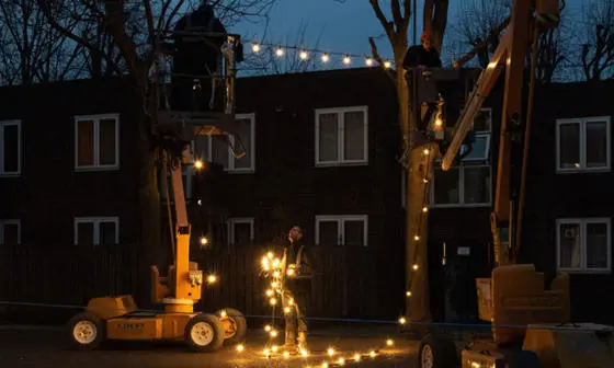 Two workers put up Christmas lights outside flats at dusk