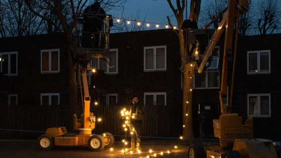 Two workers put up Christmas lights outside flats at dusk