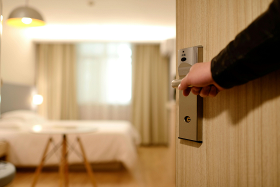 Hand opening hotel room door with key card, revealing modern room interior with warm lighting