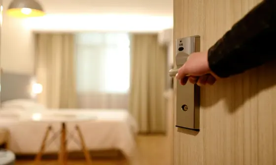 Hand opening hotel room door with key card, revealing modern room interior with warm lighting