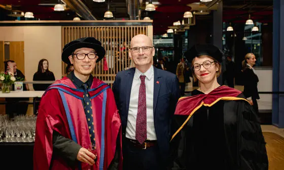 Hyun Bang Shin, Giles Atkinson and Kasia Paprocki smiling and wearing graduation robes in LSE's Centre Building.