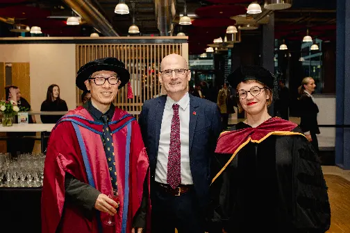Hyun Bang Shin, Giles Atkinson and Kasia Paprocki smiling and wearing graduation robes in LSE's Centre Building.