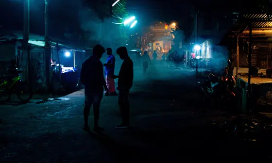 A dark street with bright lights illuminating silhouettes.