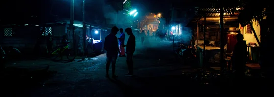 A dark street with bright lights illuminating silhouettes.