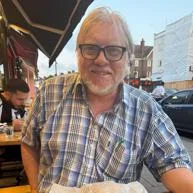 David Lowry eating outside. He is wearing a checked shirt and glasses.