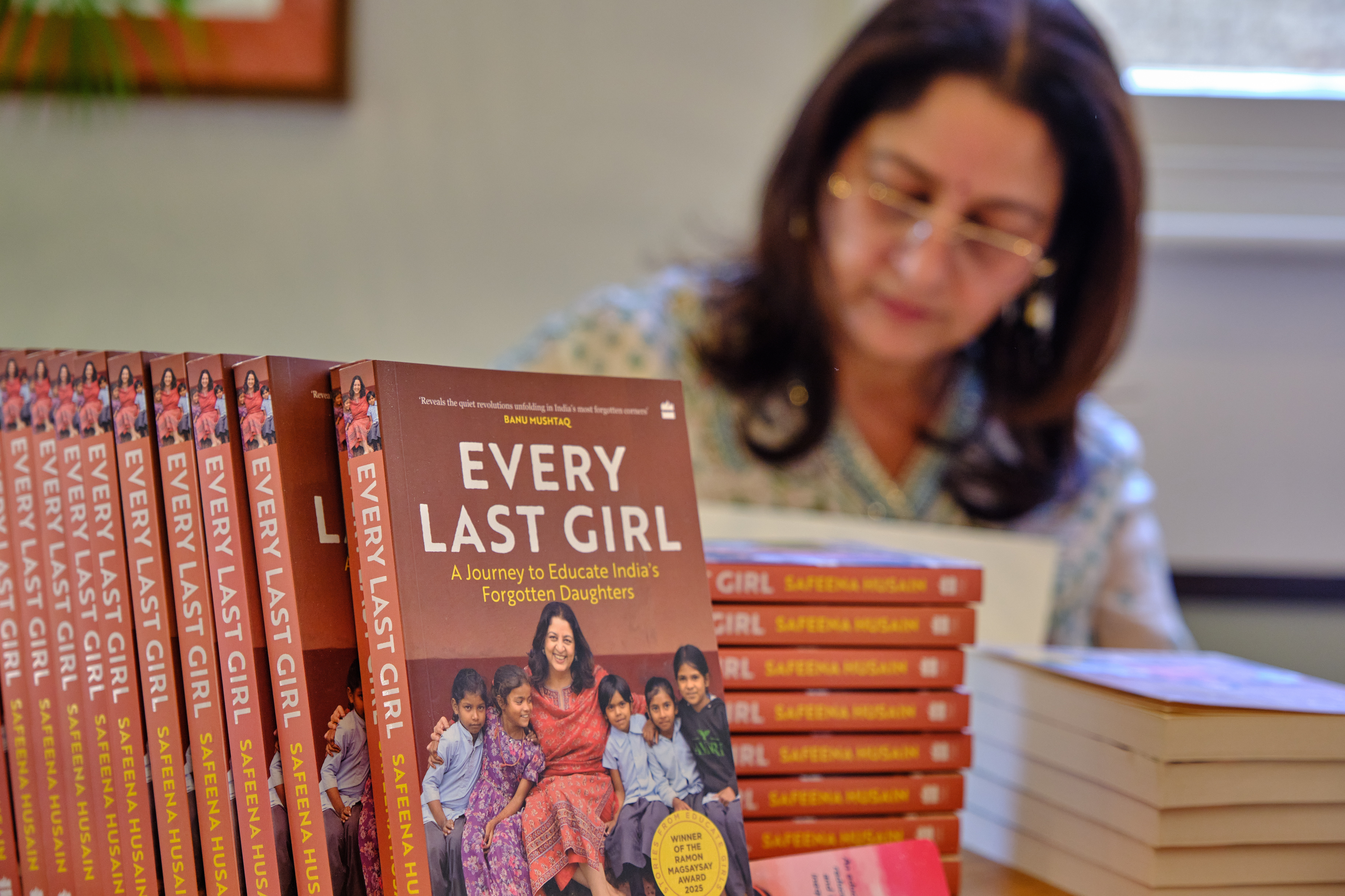 In the foreground: a stack of Safeena Husain's book every last girl: a journey to educate India's forgotten daughters. In the background: Safeena is signing books