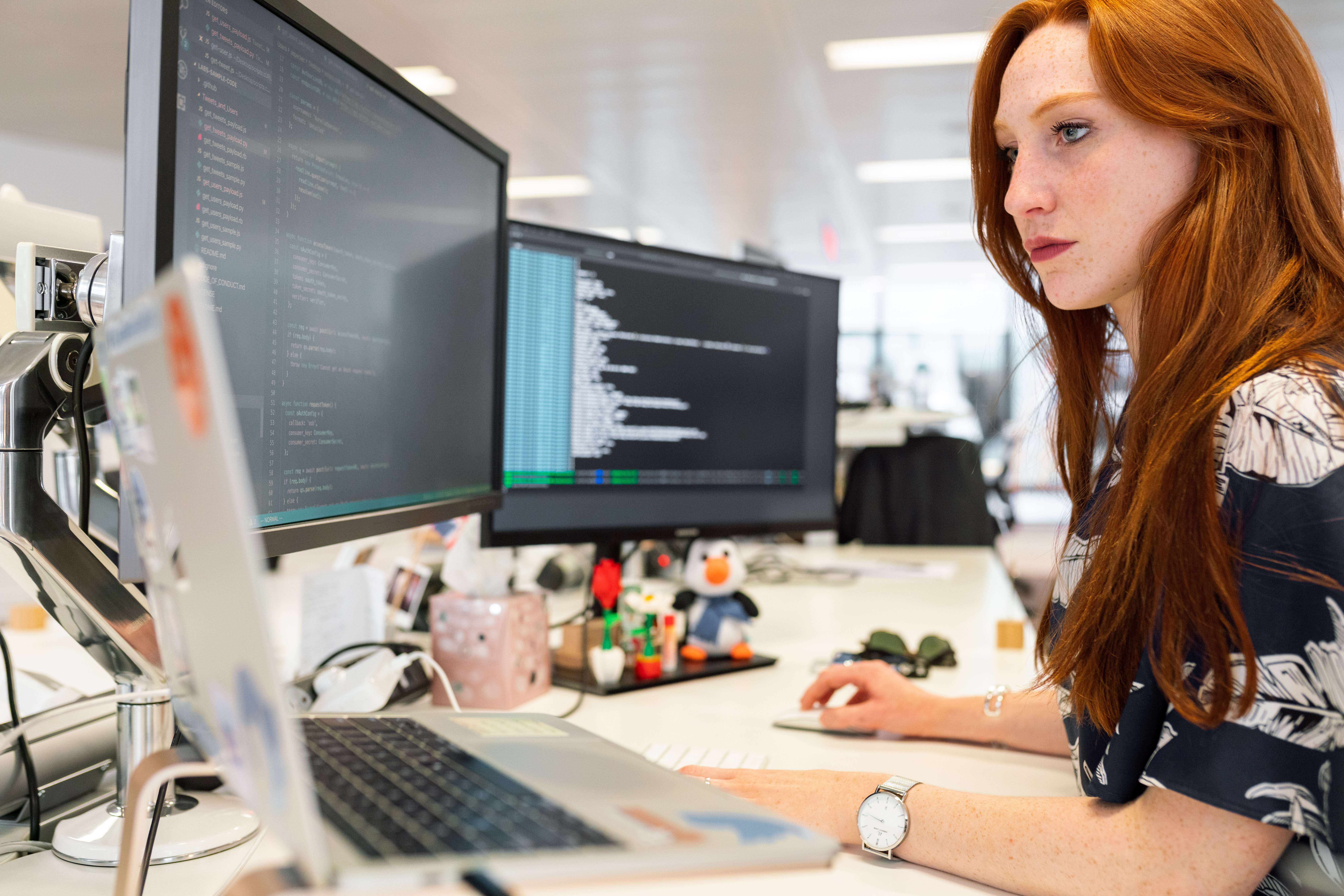 Woman sits at a desk with three screens