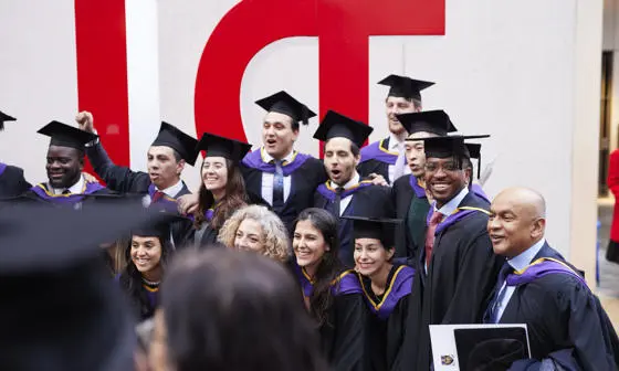 Students in graduation caps and gowns standing in front of the red LSE sign