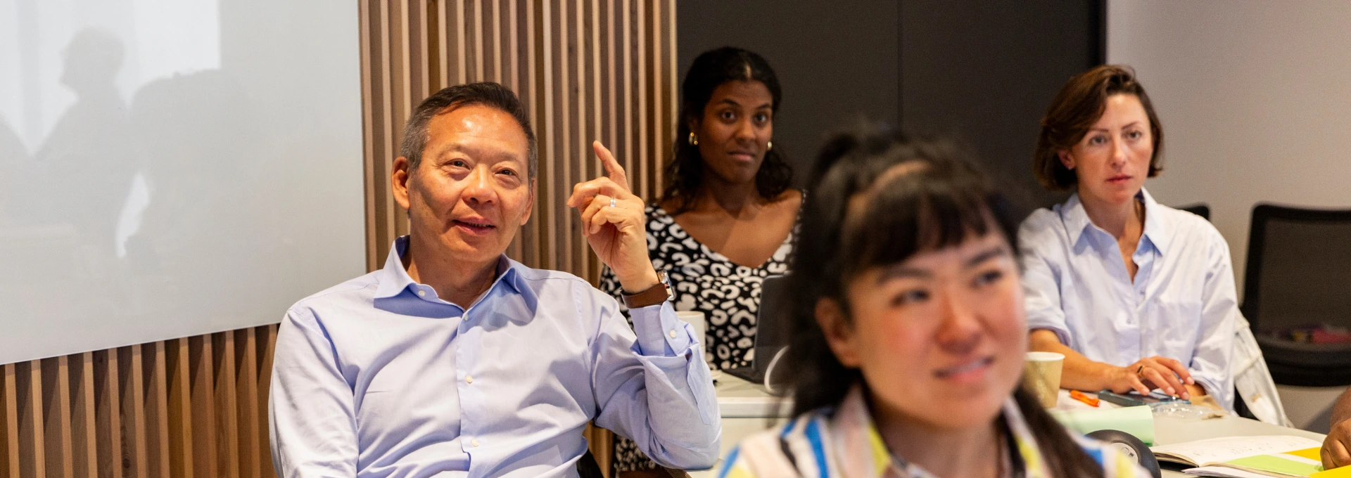 Diverse group of EMSBE students engaged in classroom discussion at LSE, with participants seated around a table in a modern learning environment.