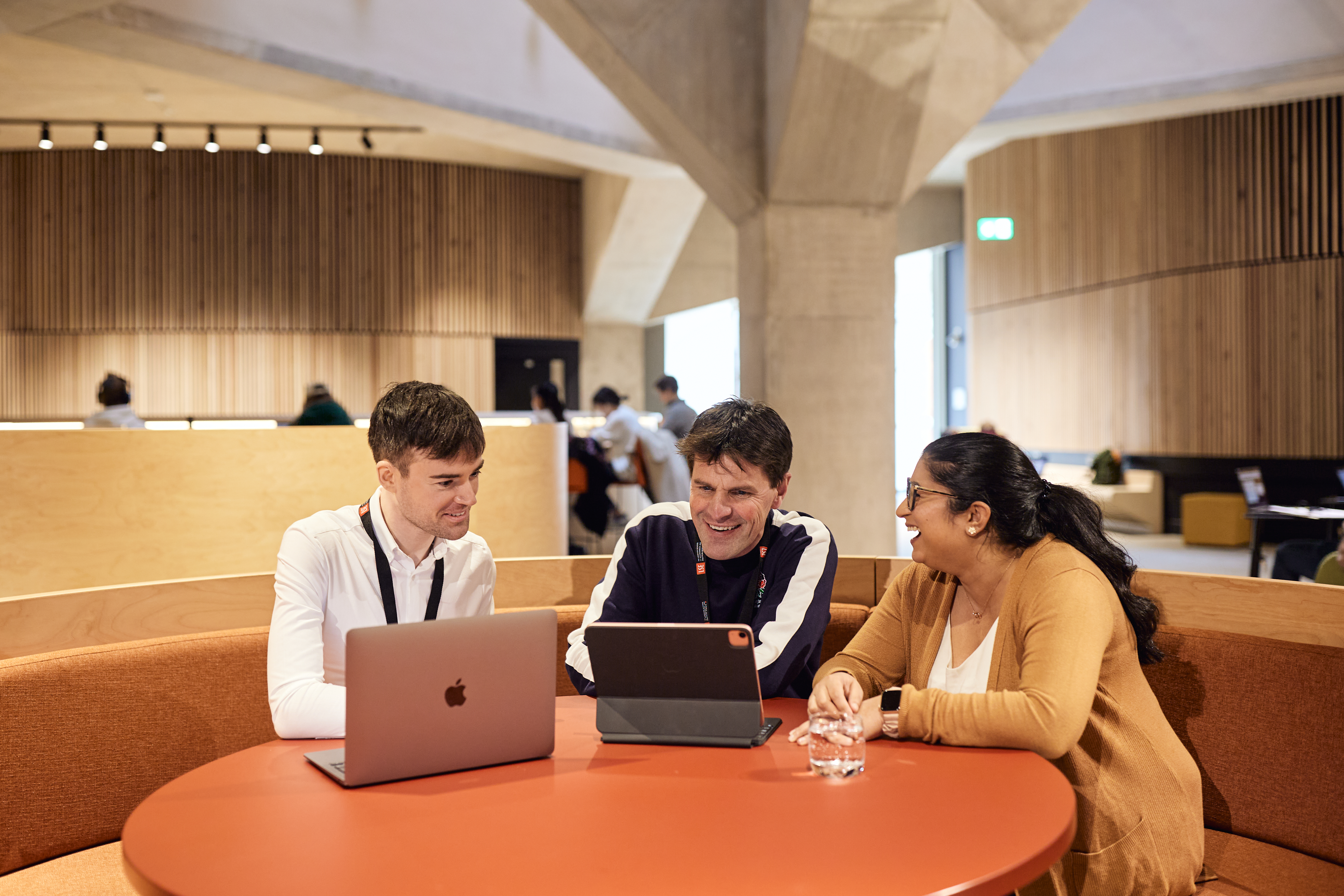 Three EMSBE students collaborating with laptops at a round table outside lecture theatre.