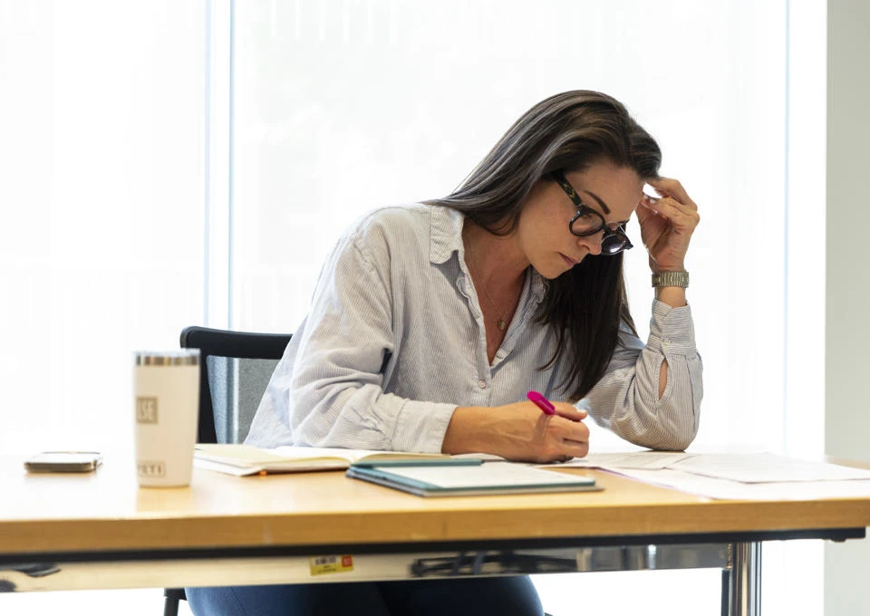 EMSBE female student writing notes at a desk with a coffee cup and notebooks in a bright, minimalist workspace.