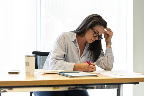 EMSBE female student writing notes at a desk with a coffee cup and notebooks in a bright, minimalist workspace.