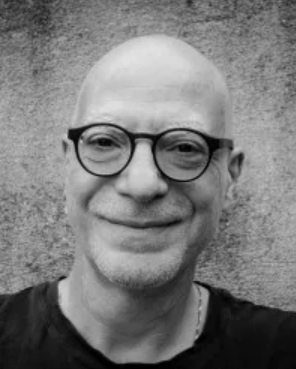 A black and white photo of Engin Isin. He is wearing glasses and smiling.