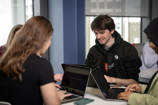 Student working on laptop with other students