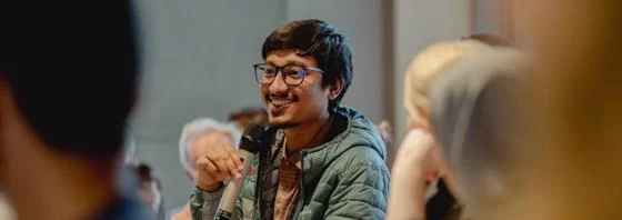 Audience member with glasses smiling and holding a microphone at an LSE event.