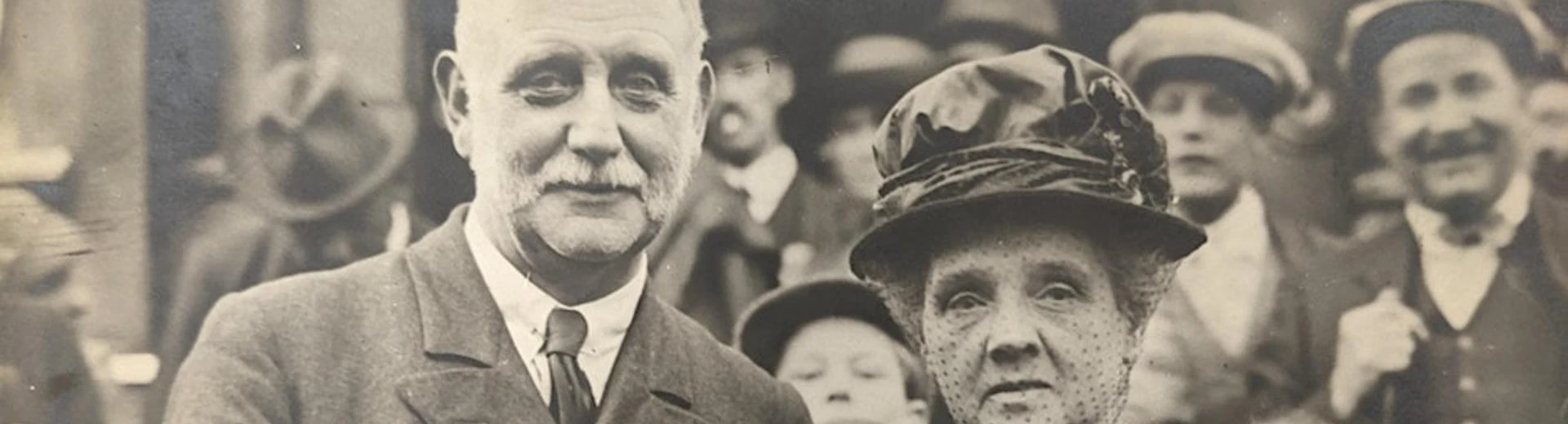 George Lansbury stood with his wife for a photograph. Behind them is a crowd of people.