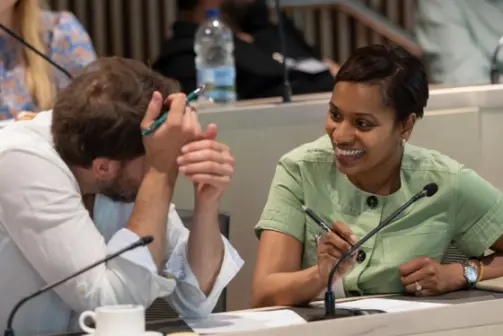Two professionals in discussion during a seminar, smiling and taking notes in a classroom setting.