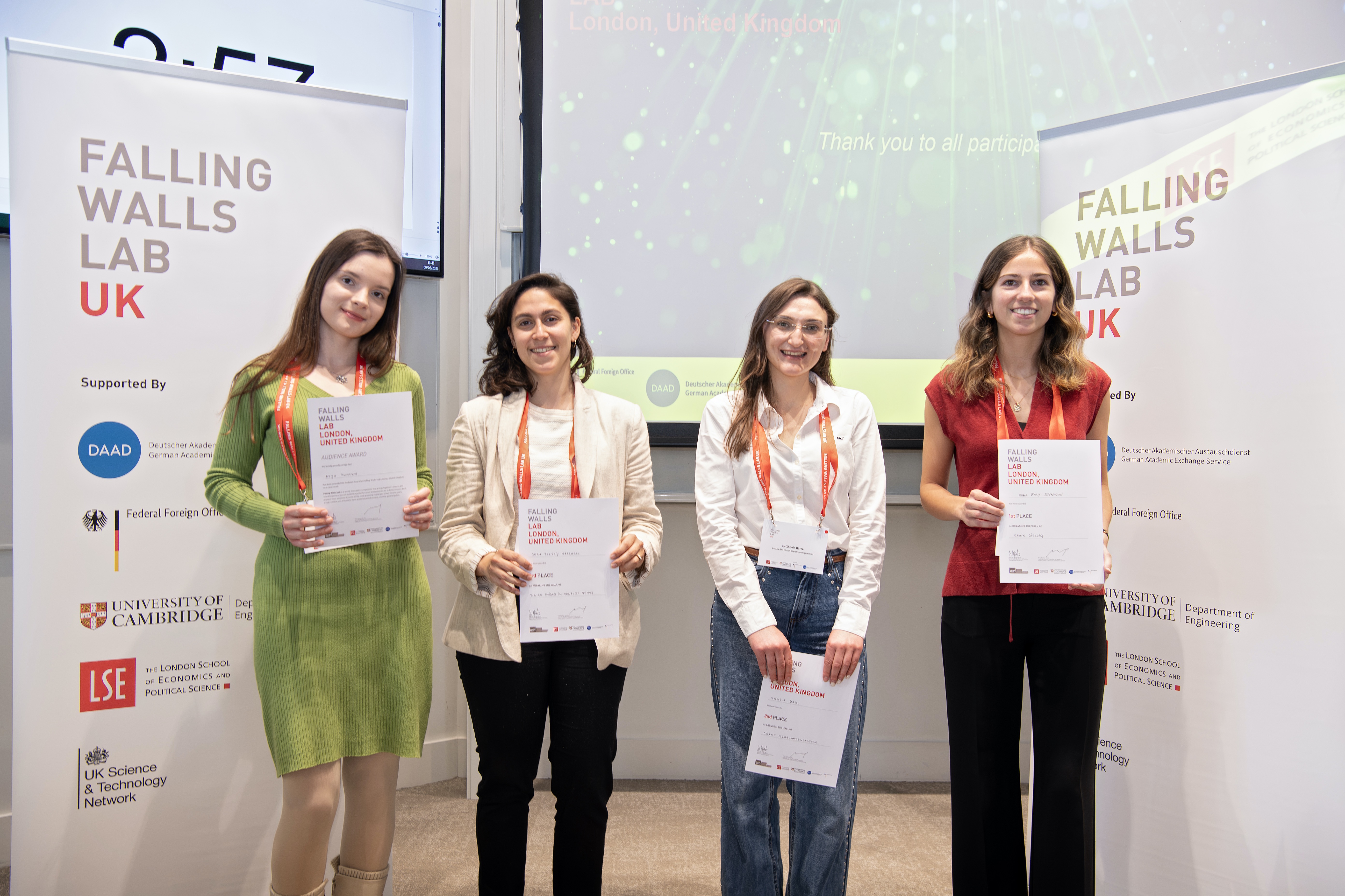 The group of commended presenters standing in front of the Falling Walls Lab UK signs with their certificates, from left to right: Asja Puncuh, Sera Tolgay Marshall, Dr Xhoela Bame and María Jenkinson Álvarez.