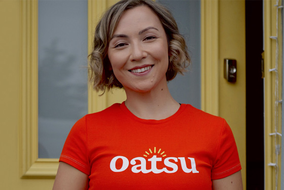 Lauren O'Donnell stands beside a yellow door wearing a red Oatsu branded t-shirt