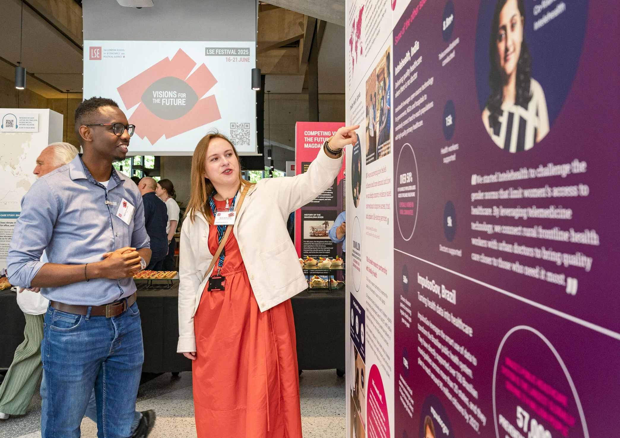 Woman points at LSE Festival display board exhibition next to a man